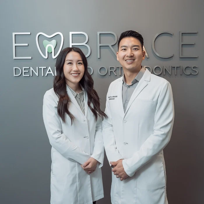 Drs. Christina S Lee and Peter Lee standing in front of a sign for Embrace Dental and Orthodontics